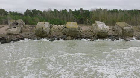 vista aérea de establecimiento de edificios de fortificación junto al mar abandonados en los fuertes del norte de karosta, costa del mar báltico, grandes olas, día nublado, cámara lenta, drone rodante disparado a la derecha