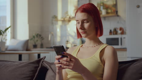 young red-haired woman using mobile phone on couch at home