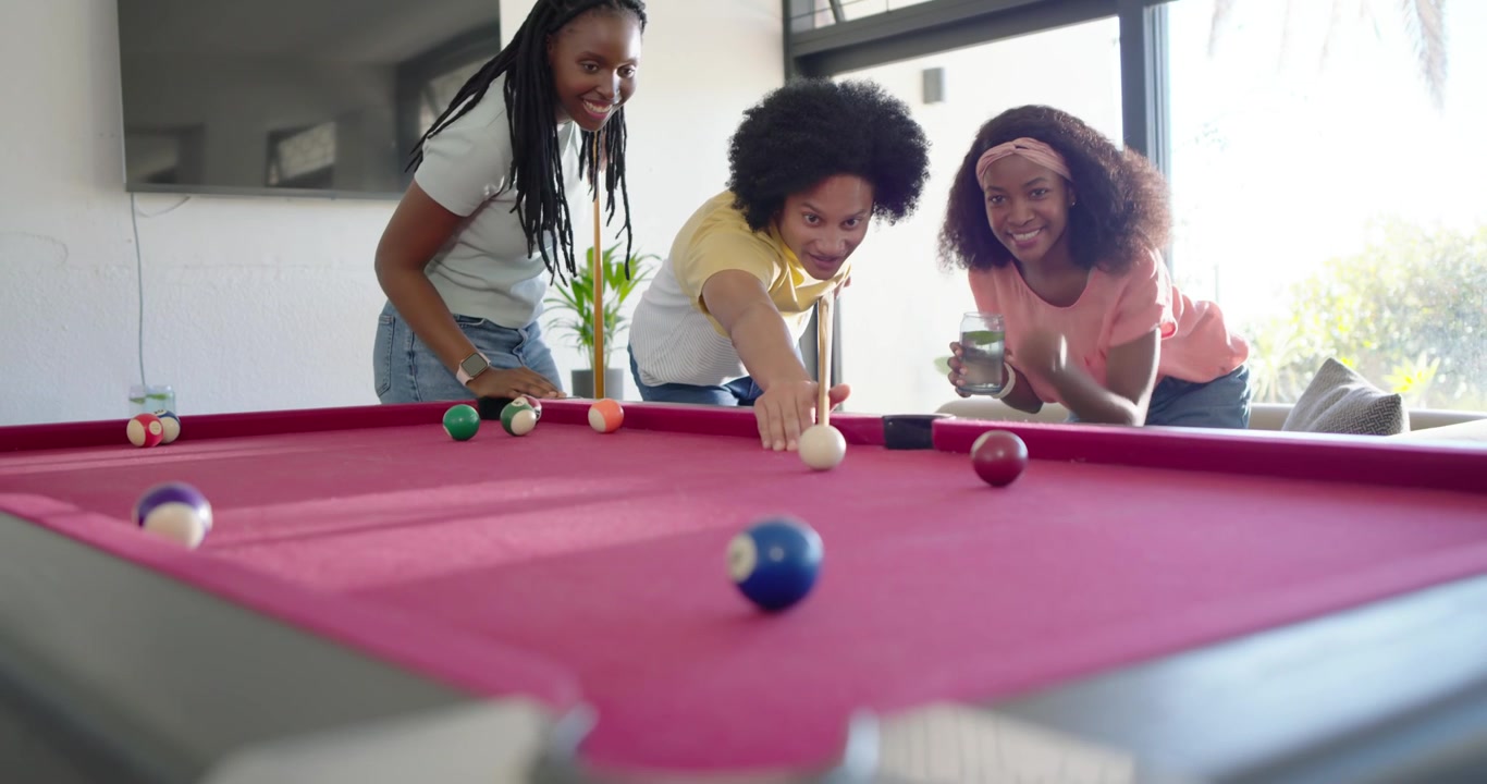 Friends studying pink felt pool table balls for game at home, man tapping cue, cheering