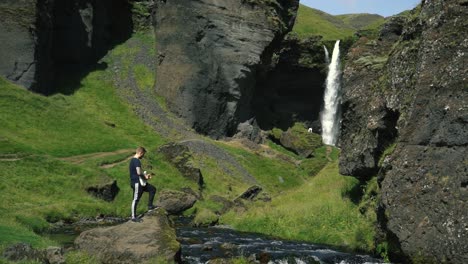 hombre tocando la guitarra frente a una hermosa cascada en islandia-12