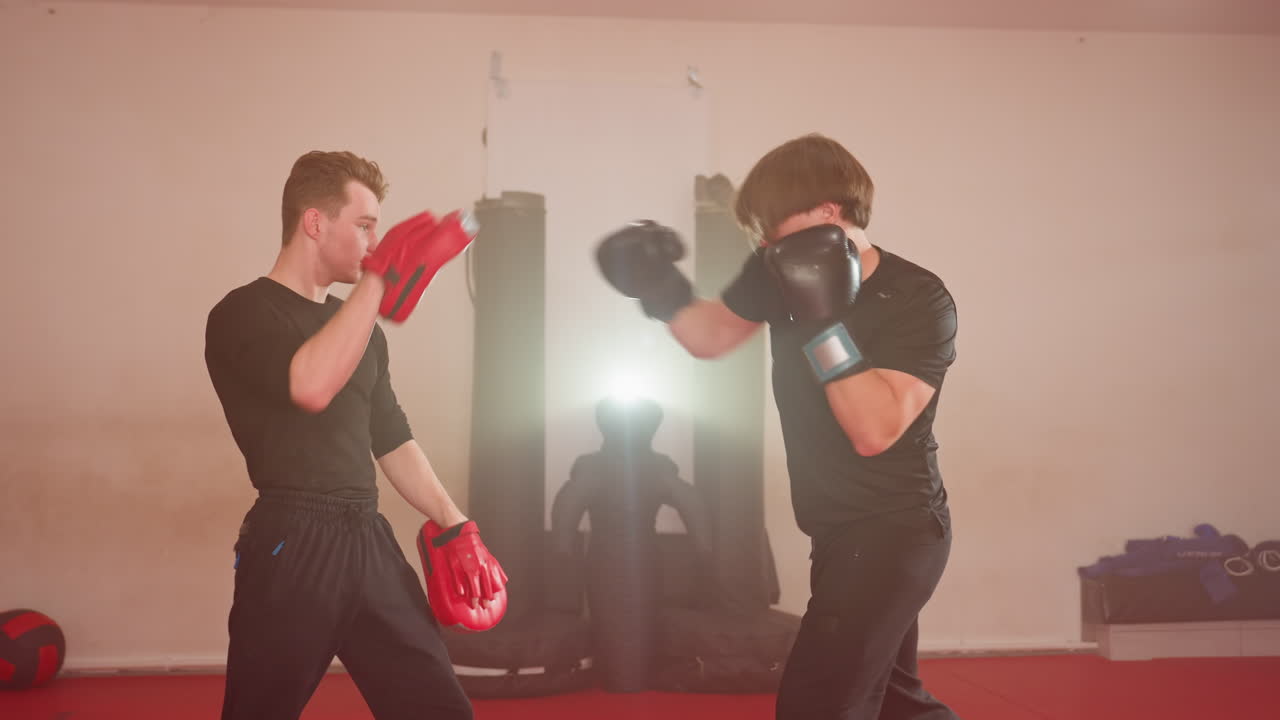 MMA fighters face each other during training session inside gym, wearing protective gloves and pads, preparing for sparring practice, focusing on combat technique, mental toughness in martial arts environment