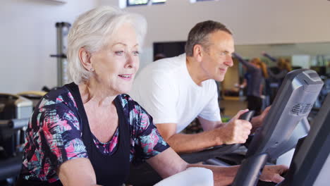 Pareja-Senior-Activa-Haciendo-Ejercicio-En-Máquinas-De-Ciclismo-En-El-Gimnasio