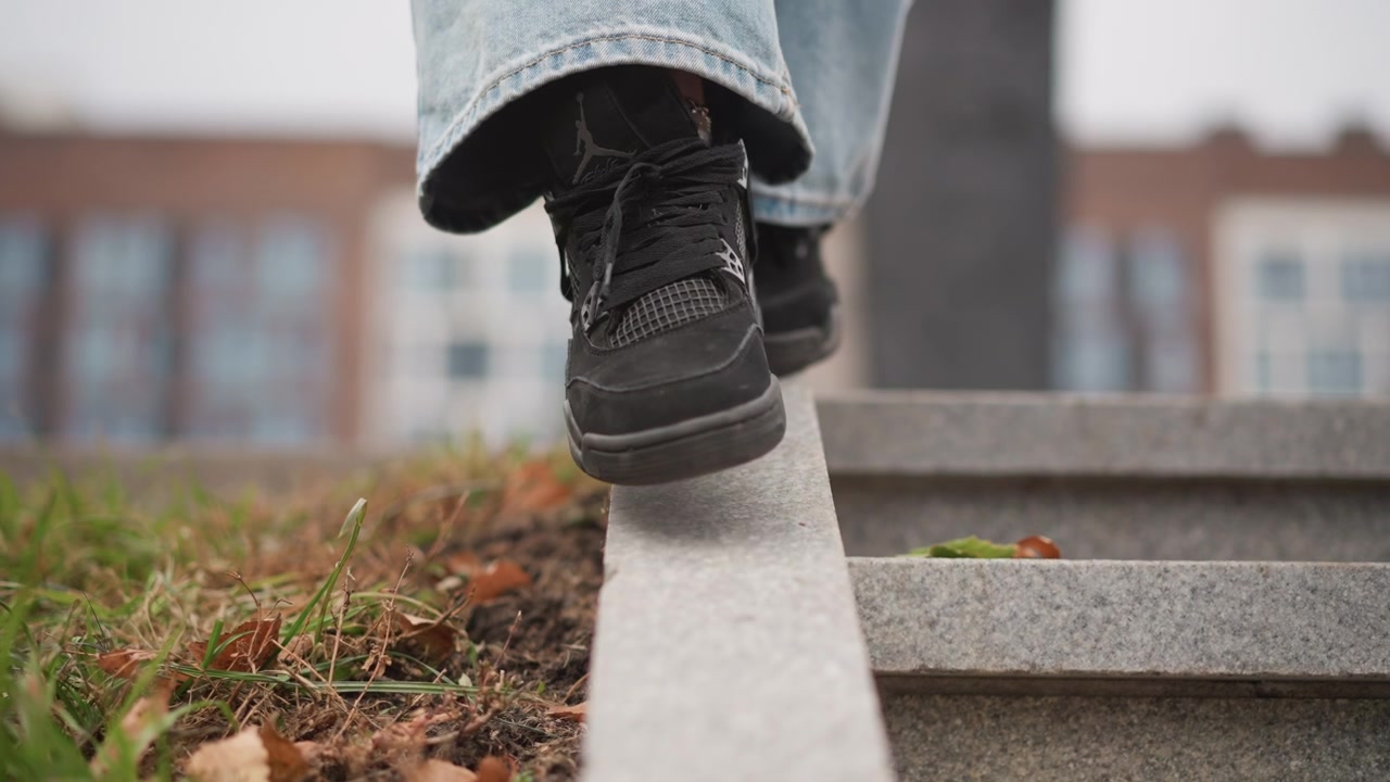 Close up of person feet in black sneakers and blue jeans carefully stepping along narrow edge of concrete steps. focus remains on foot movement with visible texture details like shoe