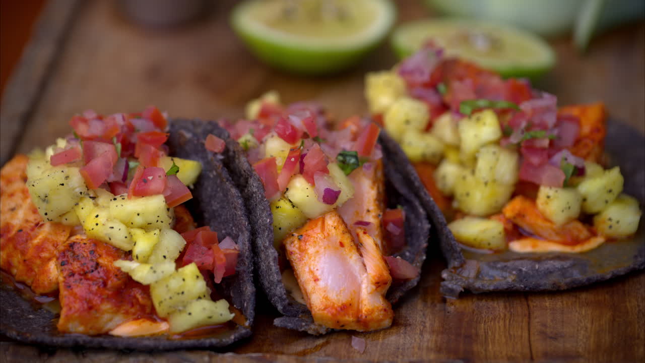 Primo piano al rallentatore di una variante dei tradizionali tacos al pastor messicani, preparati con salmone marinato su tortillas di mais blu e ananas
