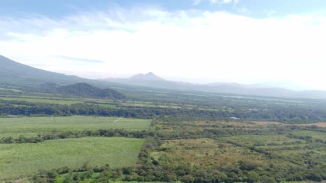 un volcán lejano se eleva sobre vastos campos verdes y bosques bajo un cielo brillante y nublado en guatemala.