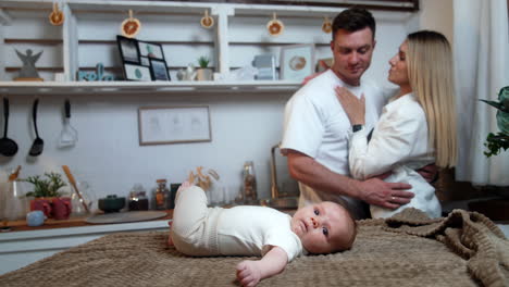 mother and father with their newborn son in the kitchen. happy parents embrace looking at their baby.