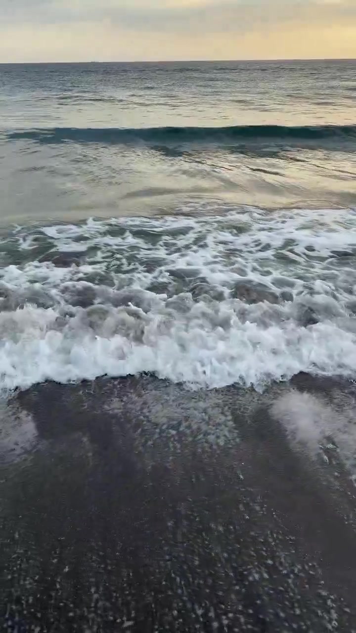 Dolci onde dell'oceano che si infrangono su una spiaggia di sabbia scura al tramonto