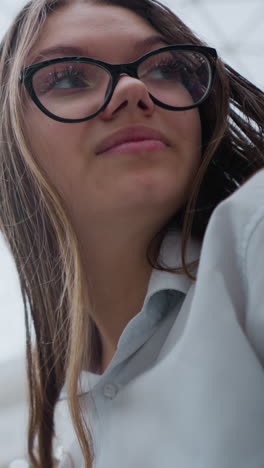 up de la dama en la escalera mecánica con gafas mirando contemplativa, enmarcado contra un techo interior moderno, reflejando la expresión reflexiva en un entorno urbano