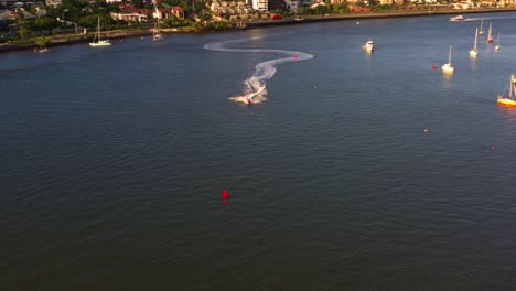 Luftschwenkansicht,-Einem-Jetski-Folgend,-Der-Auf-Dem-Fluss-Von-Hamilton-In-Richtung-Newstead-Rast.-Blick-Auf-Den-Wohnkomplex-Am-Nördlichen-Flussufer-Bei-Sonnenuntergang,-Goldene-Stunde,-Brisbane-City,-Queensland