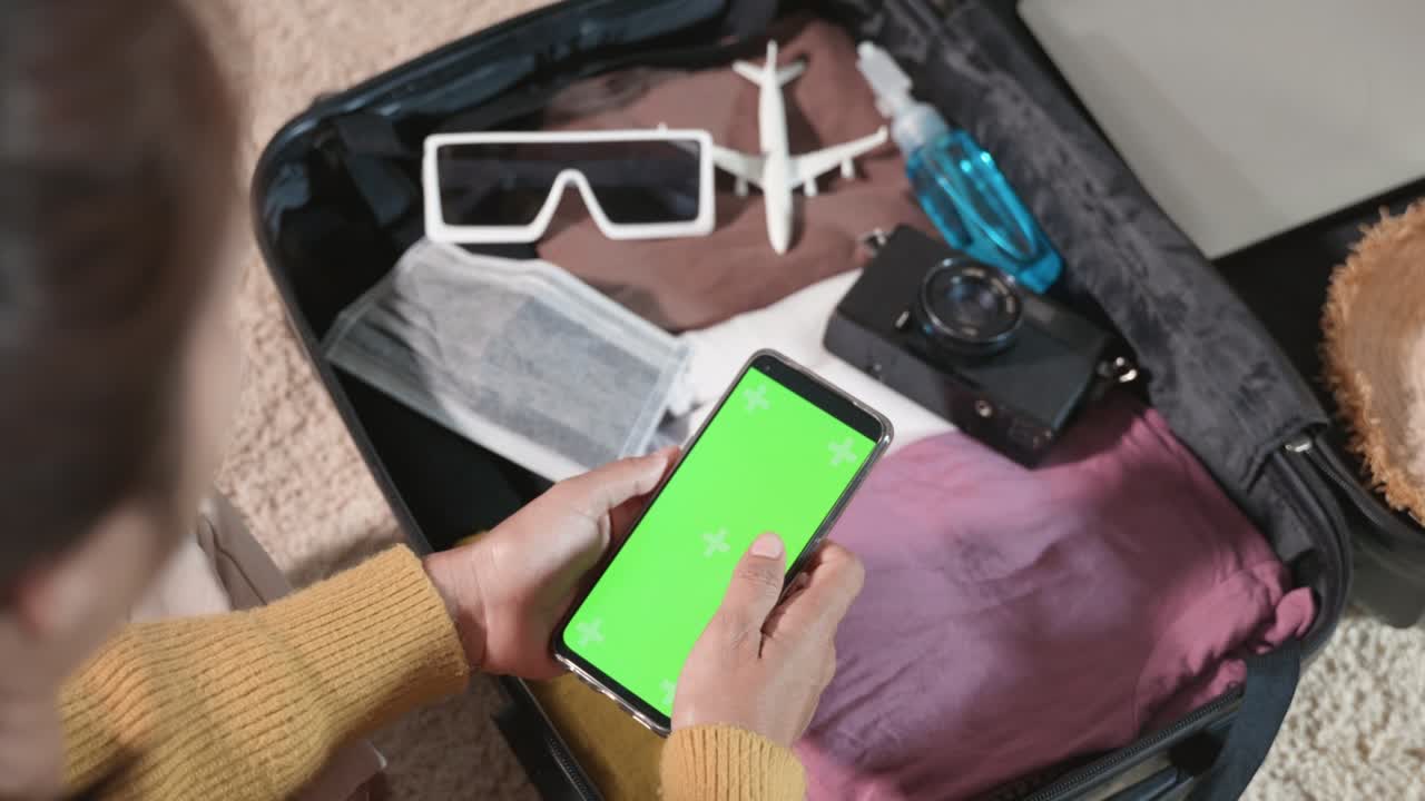 mujer usando una pantalla verde en blanco de su teléfono inteligente y empacando una bolsa de maletas para un viaje de viaje de vacaciones de fin de semana en casa