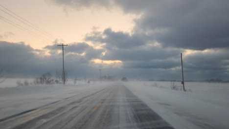 Blowing-snow-thru-windshield-of-a-vehicle-driving-on-the-frozen-and-snowy-asphalt-road-in-Toronto,-Ontario