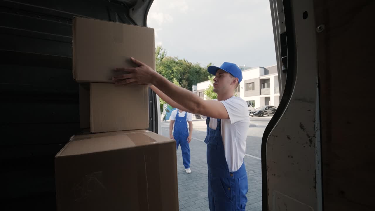 dos jóvenes trabajadores de una compañía de mudanzas están cargando cajas y muebles en un minibus