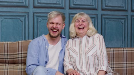 happy senior older mother and smiling young adult grown son hugging laughing looking at camera