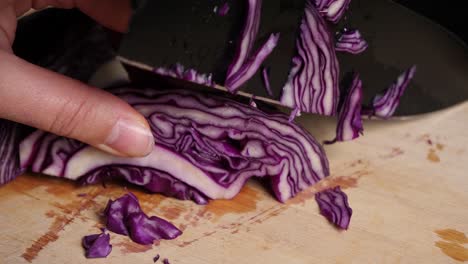 close-up cutting red cabbage with black knife on wooden chopping board