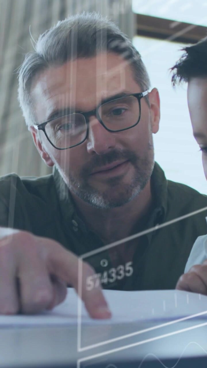 Vertical video: Dad leaning over docs pointing at line with HUD boxes appearing, teaching child