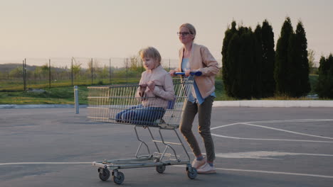 woman having fun in the parking lot at the supermarket rolls the child in the shopping trolley