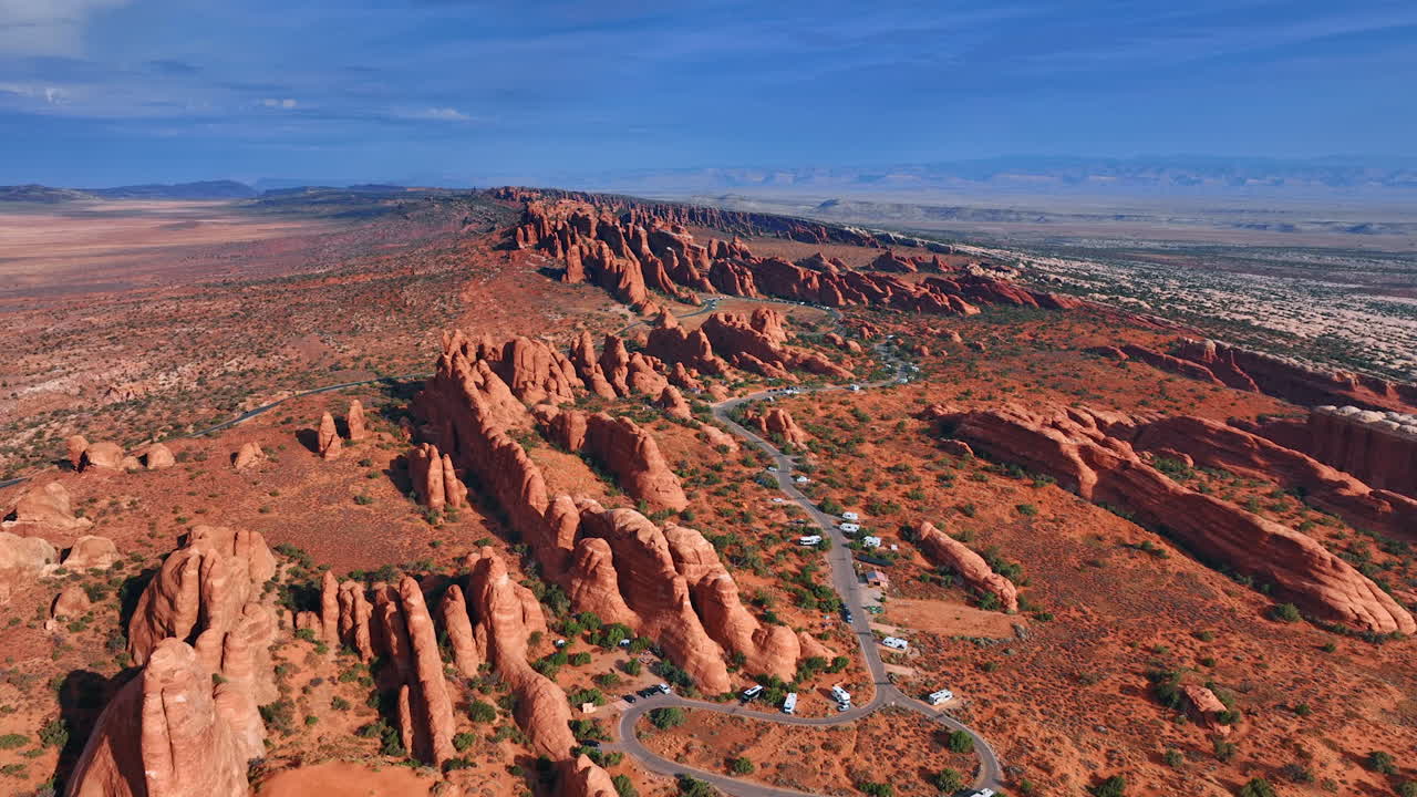 Striking scenery of the desert with whimsical rounded canyons. Numerous campervans stand parked near the highway. Camping in the Arches National Park, Utah, USA. Aerial view