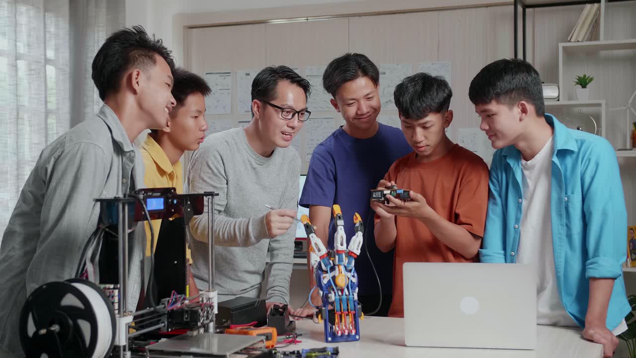 노트북, 3d 프린팅, 사이보그 손을 가진 아시아 남자가 학교에서 소년에게 회로판을 고치는 것을 가르치고 있습니다.