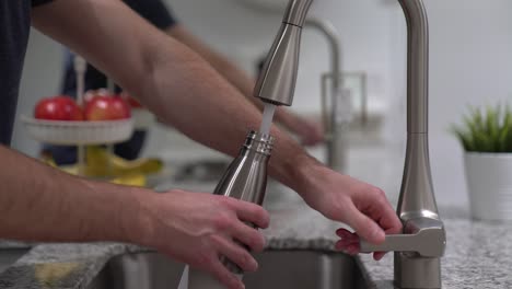 turning on sink faucet to fill up reusable water bottle with clean freshwater from kitchen tap