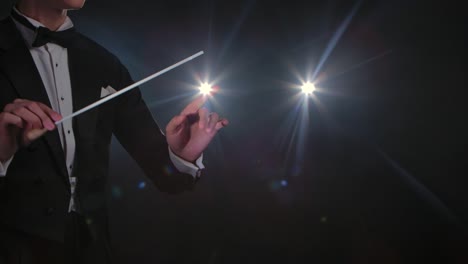 moving hands of an orchestra conductor directing musicians with movement of baton on black background with lights. conducting, directing classical musical performance with visible gestures. close up