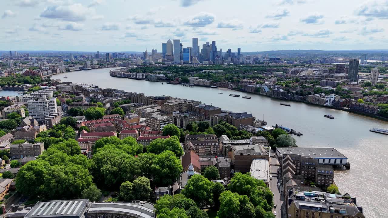 Aerial drone approach over River Thames heading east toward Canary Wharf and the Isle of Dogs, revealing a dramatic skyline of sleek, modern skyscrapers and towers.