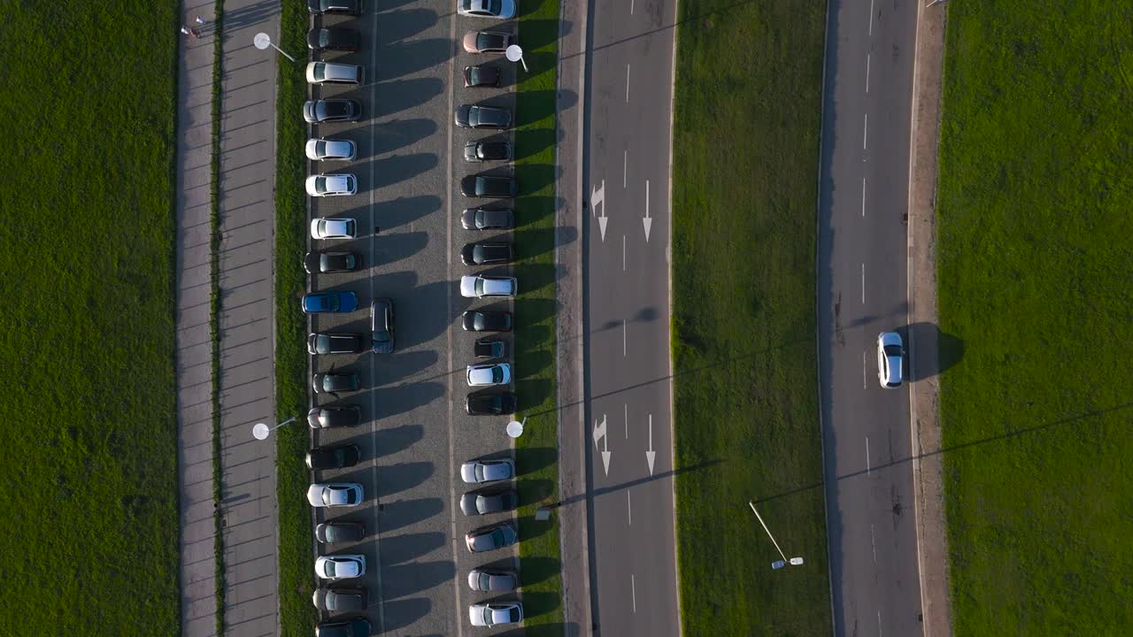 parking lot full of cars with parallel road with lane for cars, free grass separating both, top aerial drone view