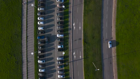 parking lot full of cars with parallel road with lane for cars, free grass separating both, top aerial drone view