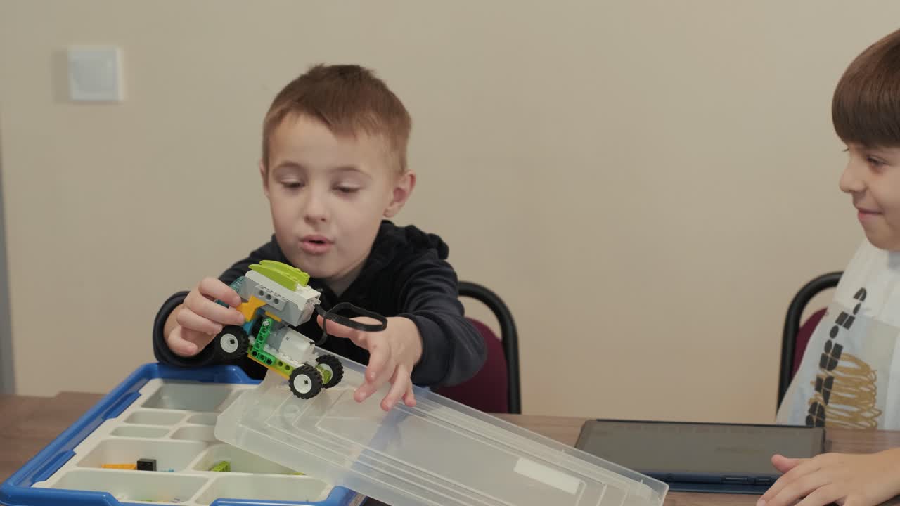 дети внимательно сосредоточились на сборке частей из робототехнического набора, с планшетом, отображающим инструкции, способствуя обучению и творчеству.