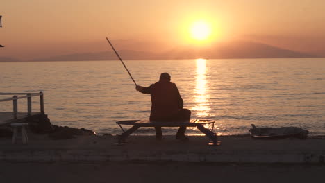 Old-Man-at-the-Promenade-sitting-on-bench-with-a-fishing-route-slow-motion