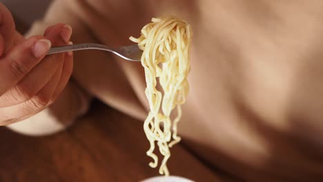 close up of a hand holding a fork with noodles on it