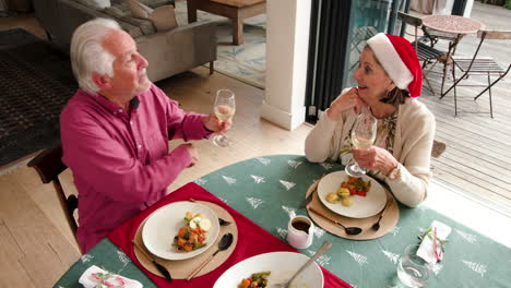 at christmas, senior couple enjoying festive meal at home, toasting with wine glasses