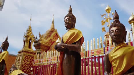 Bronze-Buddha-statue-draped-in-a-golden-robe,-standing-outdoors-with-an-ornate-temple-structure-in-the-background