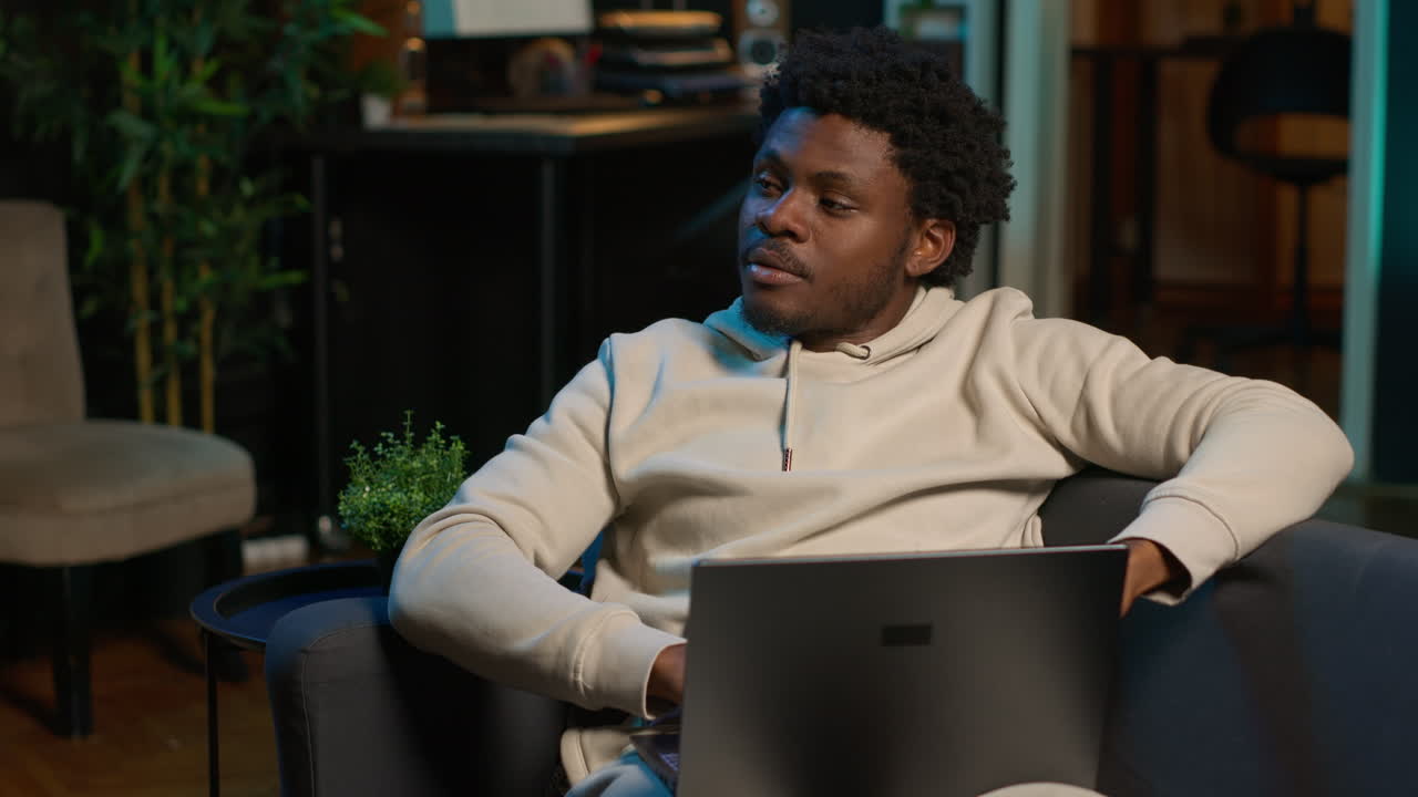 Freelancer at home focused on online research and surfing the internet, utilizing a laptop for telework and staying connected in a digital world. Browsing the social media on his couch. Camera A.