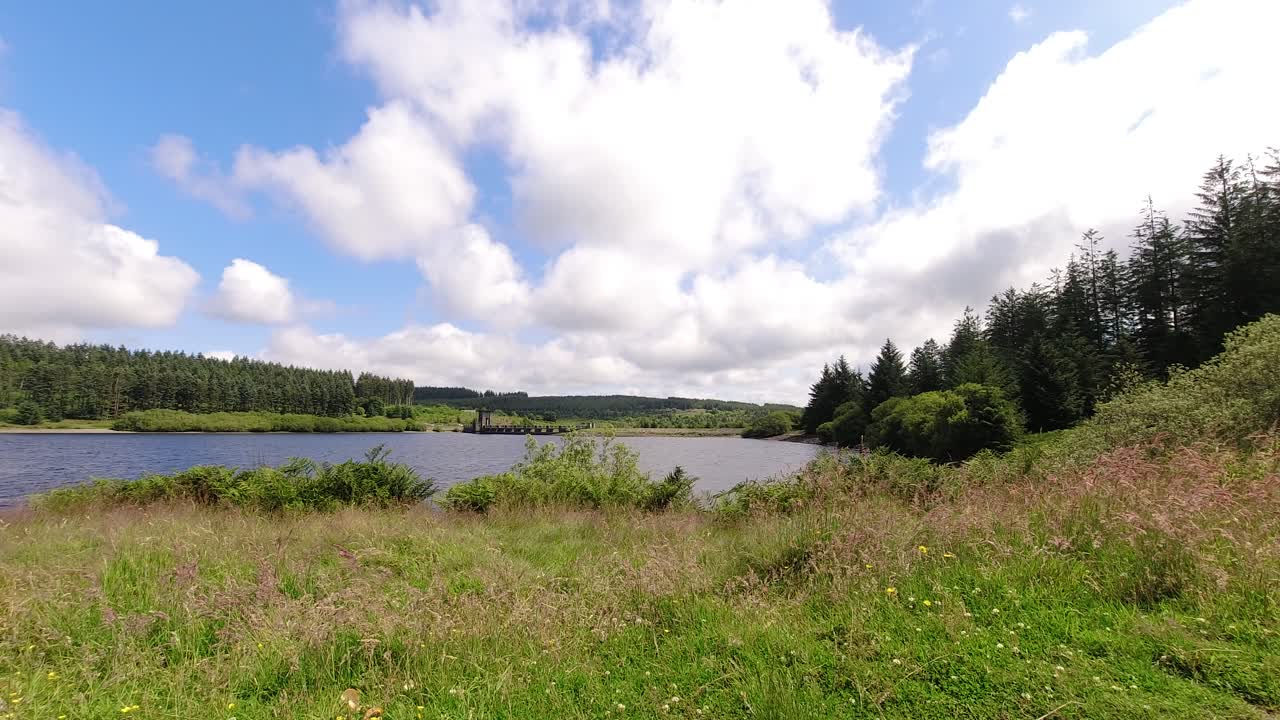 sunny alwen embalse timelapse nubes rápidas que pasan sobre el vasto agua azul del lago del bosque de izquierda a derecha