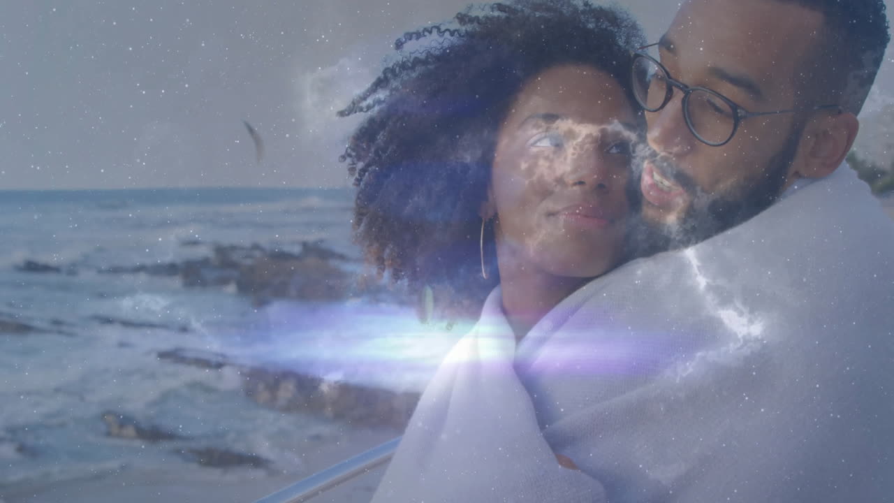 woman and man standing on coastal railing wrapping blanket, showing cosmic stars overlay for tech