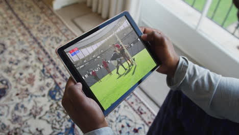 compuesto de un hombre sentado en casa viendo un partido de rugby en una tableta