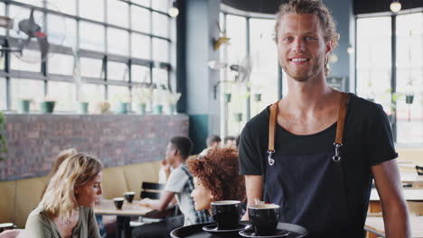 Portrait-Of-Waiter-Serving-Drinks-To-Customers-In-Busy-Cafe