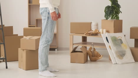 Close-Up-Of-Legs-Of-Unrecognizable-Couple-Standing-Among-Cardboard-Boxes-In-New-House
