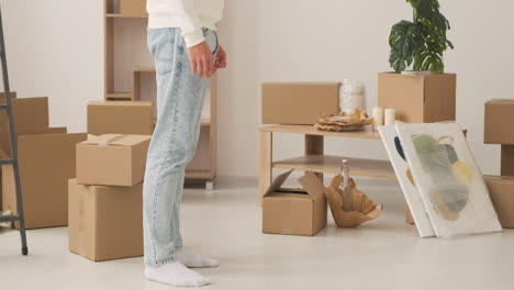 close up of legs of unrecognizable couple standing among cardboard boxes in new house