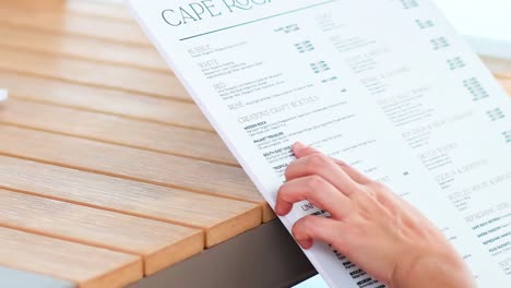 close-up of hands flipping through a drink menu on a wooden table in bright lighting.