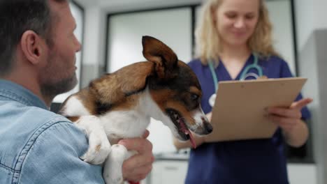 hombre caucásico sosteniendo un perro en la visita al veterinario.