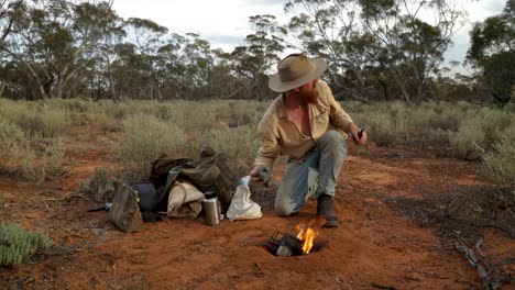 un bosquimano australiano cocina su olla de billy en un fuego en el interior