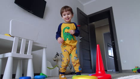 happy active kid in yellow pajama dances in his room. baby boy turns around and then falls on his knees. low angle view.
