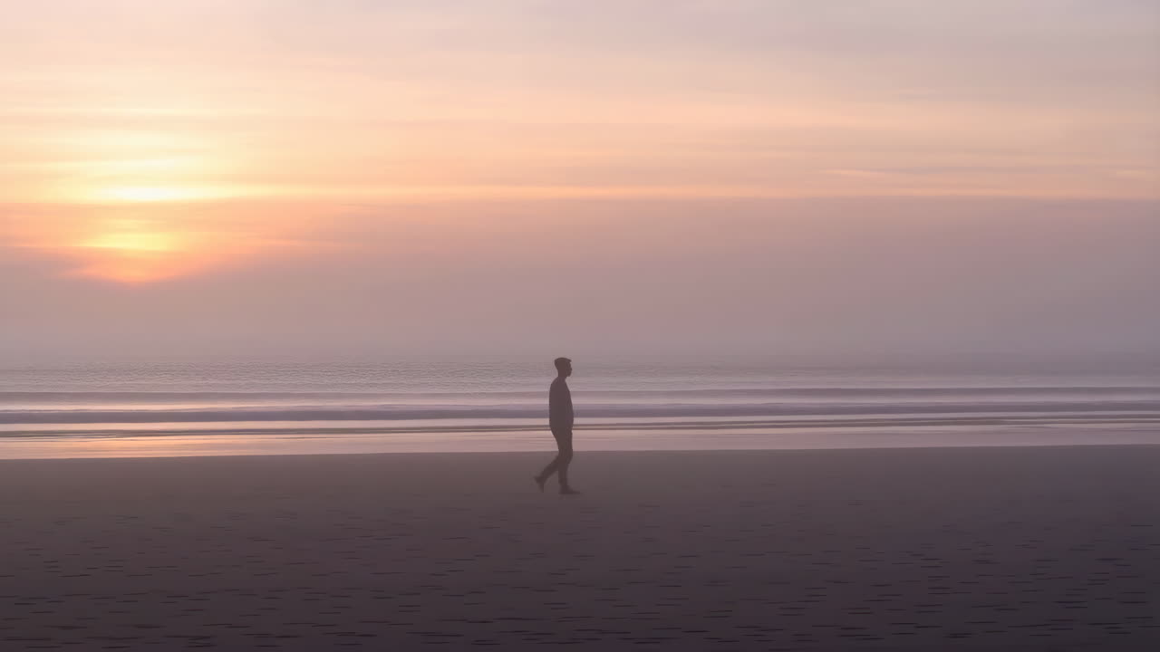Una persona che cammina su una spiaggia all'alba