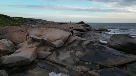 woman walks and sits on rocks of red gate beach facing ocean at sunset, western australia