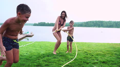 mom and son playing on the lawn pouring water laughing and having fun on the playground with a lawn on the background of his house near the lake