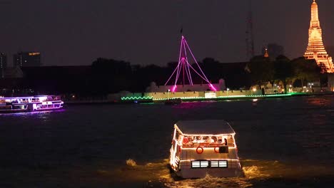 illuminated boat travels past wat arun at night