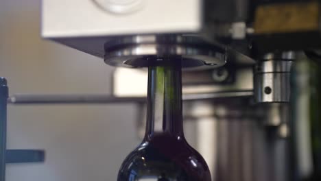 wine bottle corking machine placing caps on red wine green glass bottles, close up shot