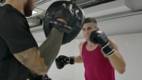 slow motion: power blow to boxing paw. strong tattooed athlete in sports clothing training on boxing paws with partner