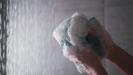 woman squeezes loofah in shower cabin closeup. lady hands hold foamy body washing sponge against water sprays. soft supply for personal hygiene